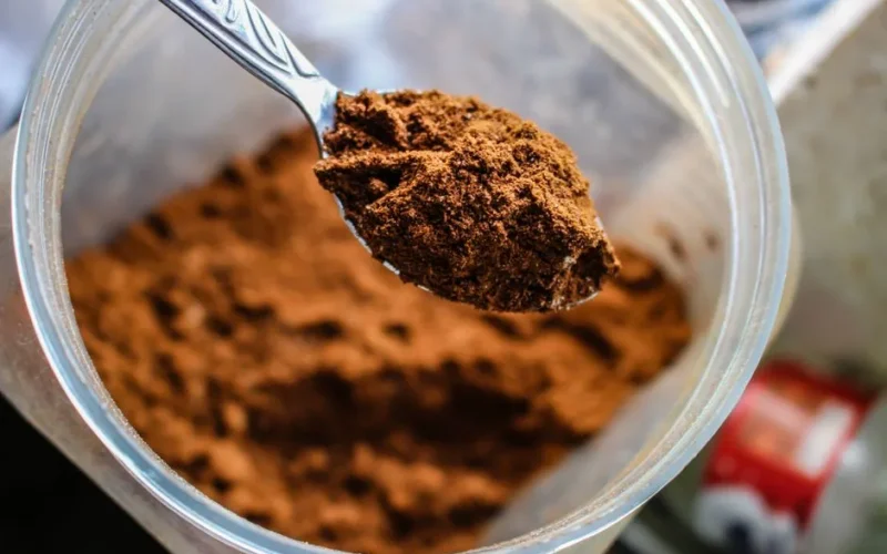 Focused shot of a spoon scooping cocoa powder from a container, emphasizing texture.