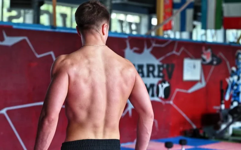 Shirtless man showcasing muscular back indoors in fitness gym.