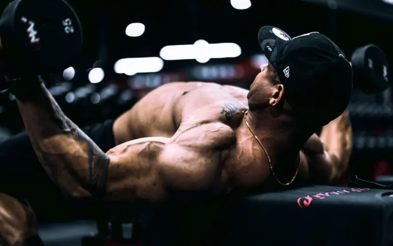 Focused athlete lifting dumbbells in an indoor gym environment, showcasing strength and dedication.