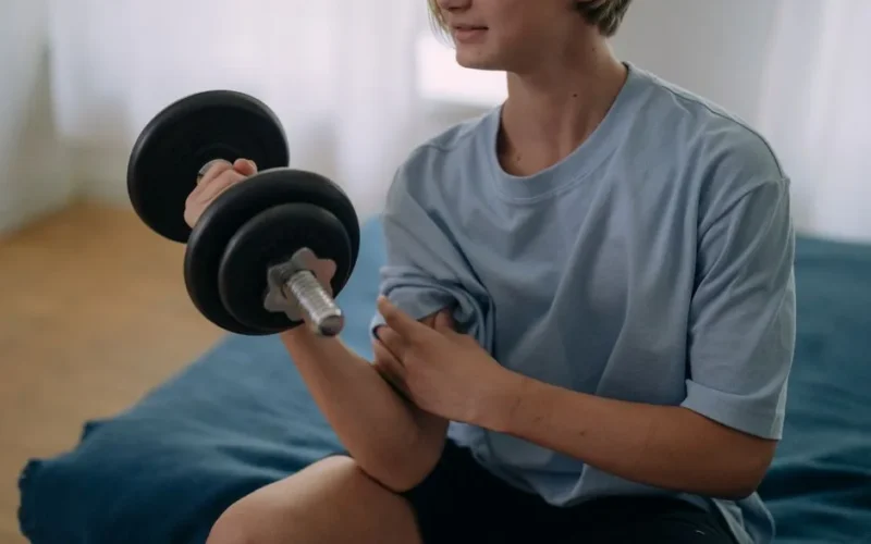 Teenage person lifting a dumbbell in a home setting, focused on fitness and health.