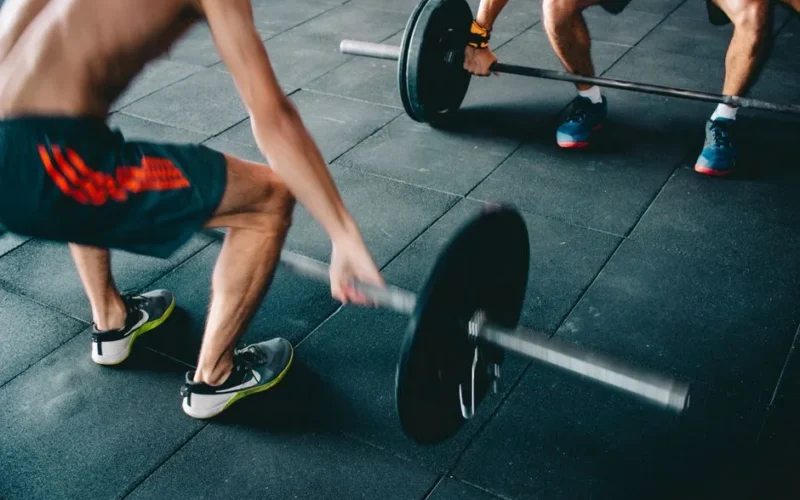Two men lifting barbells showing strength and effort in a gym setting.