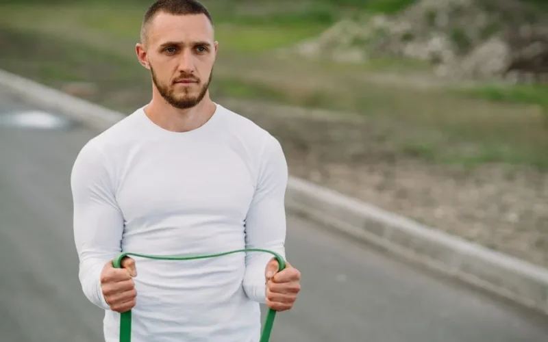 Adult man working out with a resistance band on an outdoor road.