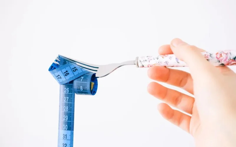 A floral-handled fork twirls a blue measuring tape, symbolizing diet and health.