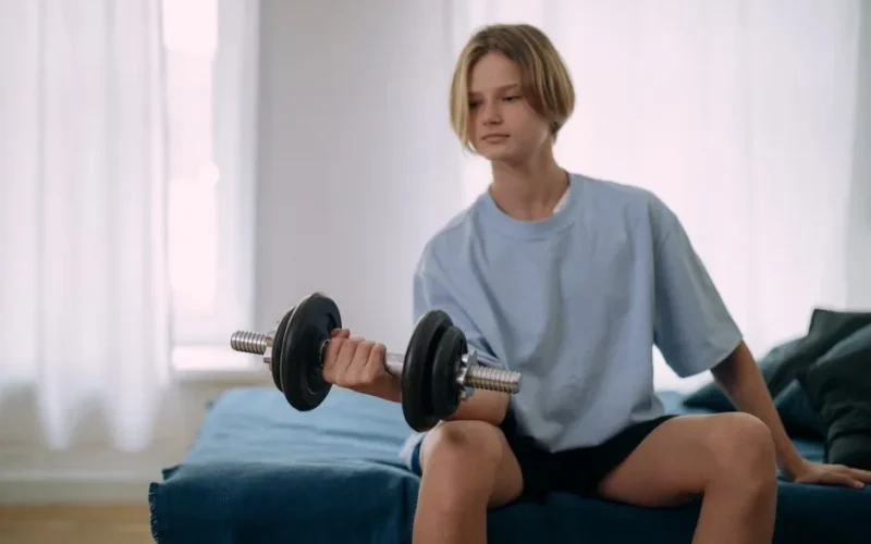 Young teen lifting dumbbells indoors, focusing on fitness and exercise at home.