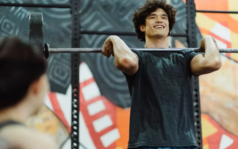 Young Asian man lifting a barbell indoors, showcasing strength and determination.