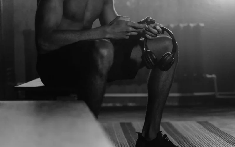 Monochrome photo of a man sitting on a gym bench holding headphones, evoking a quiet and focused atmosphere.