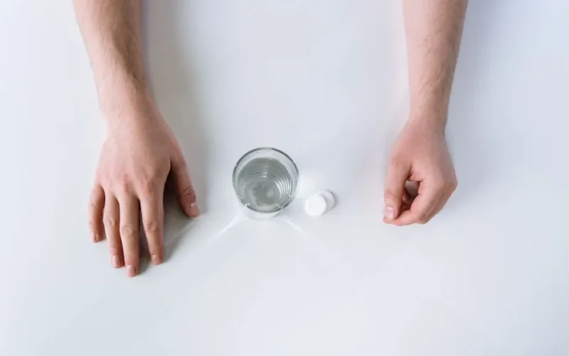 Top-down view of effervescent tablets, glass of water, and hands on a clean white background.