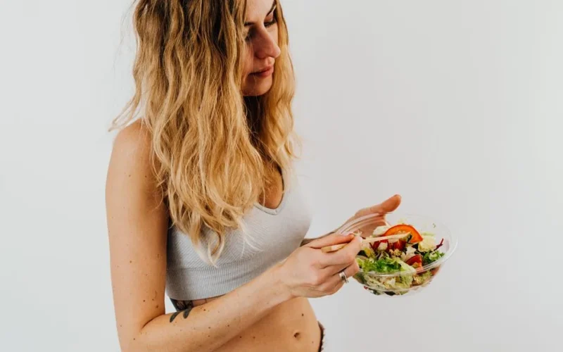 A caucasian woman in a sports bra enjoying a fresh salad, embodying healthy eating and lifestyle.
