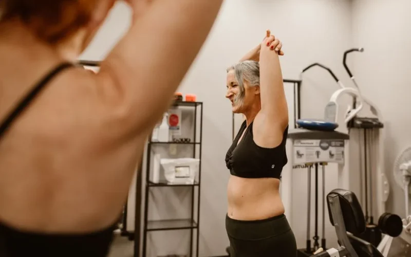A middle-aged woman confidently stretches in a gym, embracing wellness and healthy living.