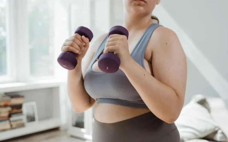 Plus size woman in activewear working out with dumbbells indoors, promoting body positivity.
