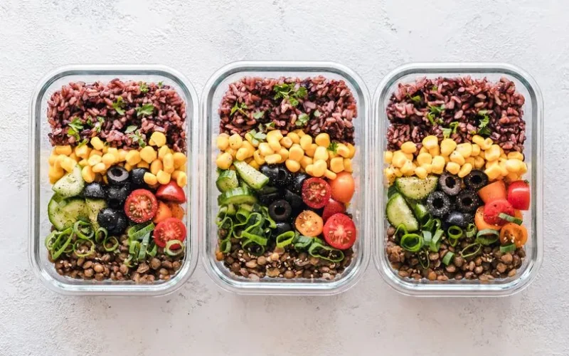 Colorful healthy meal prep with corn, olives, tomatoes, and lentils in glass containers. Perfect for mindful eating.