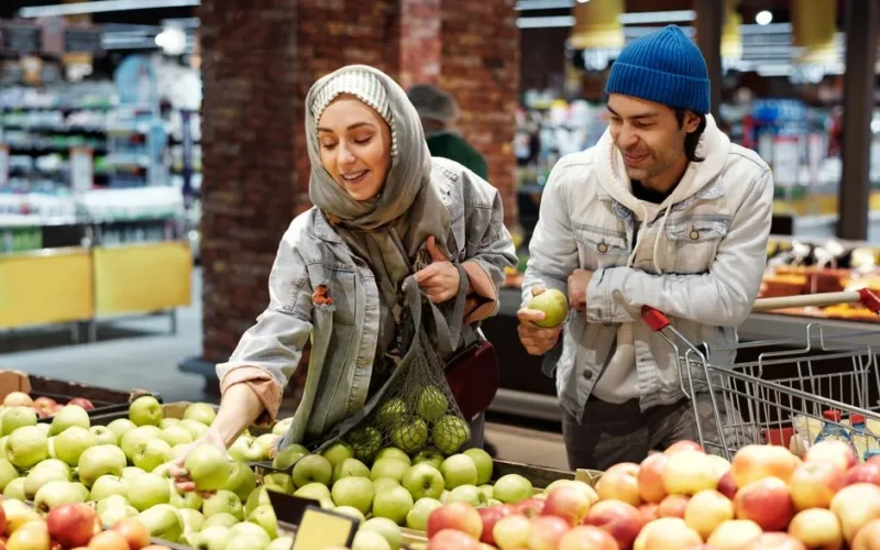 Muslim couple selects fresh apples at a supermarket, enjoying a shopping experience.