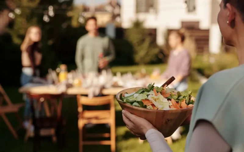A person holding a fresh salad bowl at an outdoor family gathering.