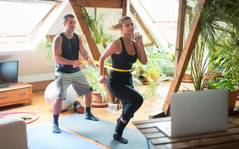 A couple working out on yoga mats indoors, using a laptop for guidance.