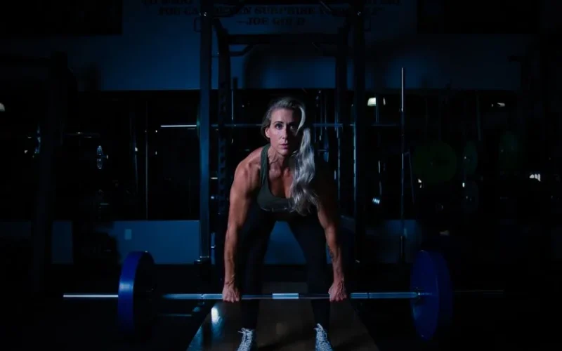 A fit woman lifting a barbell in a dimly lit gym, showcasing strength and determination.