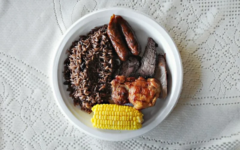 A mouthwatering platter of grilled meat, rice, and corn on a lace tablecloth.