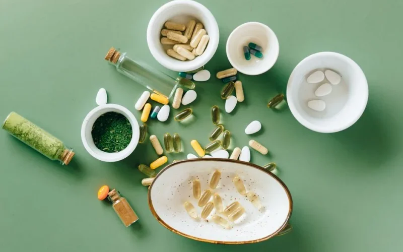 Top view of various herbal and pharmaceutical supplements in ceramic bowls on a green background.