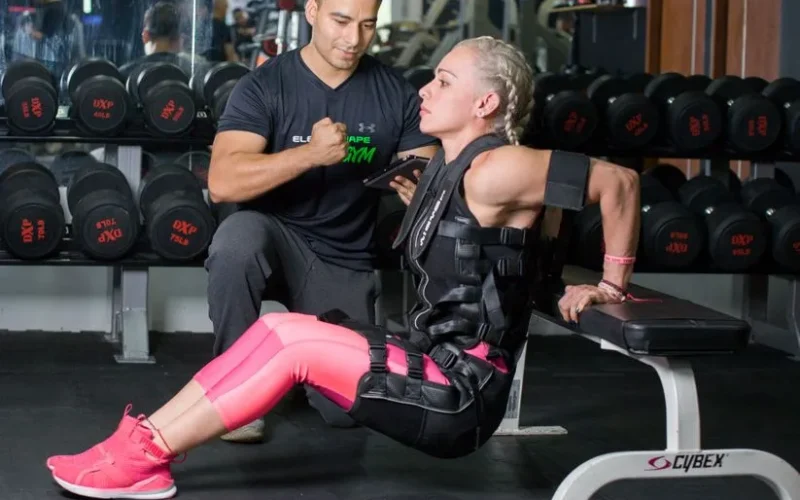 Woman doing tricep dips with personal trainer support in a gym setting.