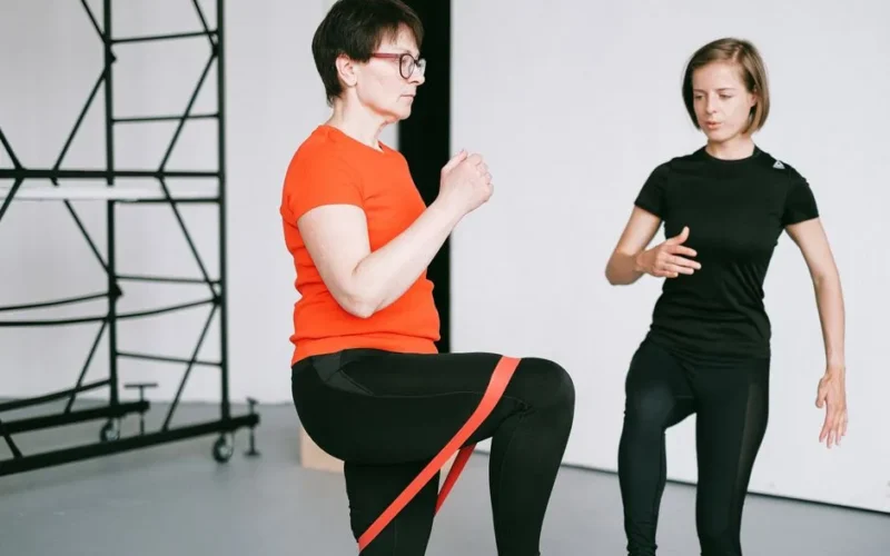 Personal trainer guiding a woman with resistance band exercise in a gym setting.