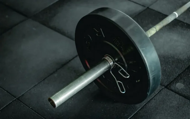 Detailed view of a barbell with heavy weights resting on a dark gym floor mat.